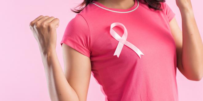 A woman wearing a breast cancer ribbon and flexing her muscles