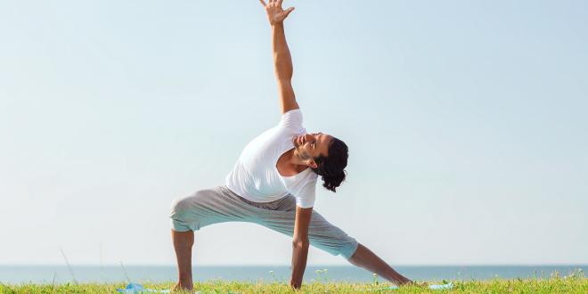 Smiling man doing yoga in the grass.