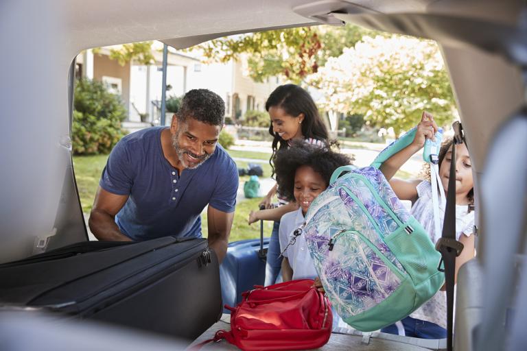 a family packing the car for a vacation, including a red bag